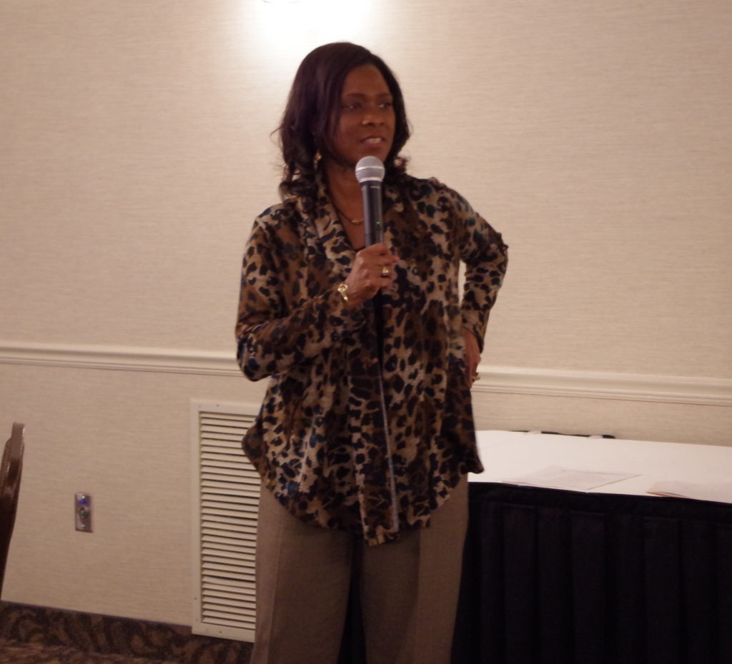 Dr. Sharon Kherat, keynote speaker, holding microphone and wearing cheetah print shirt.
