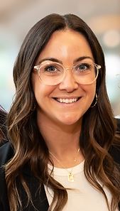 In this headshot picture of Jessica, she has long dark brown hair with waves. She is wearing clear rimmed glasses and a vibrant smile. 